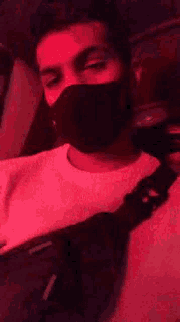 a man wearing a mask is sitting in a car with a red background .