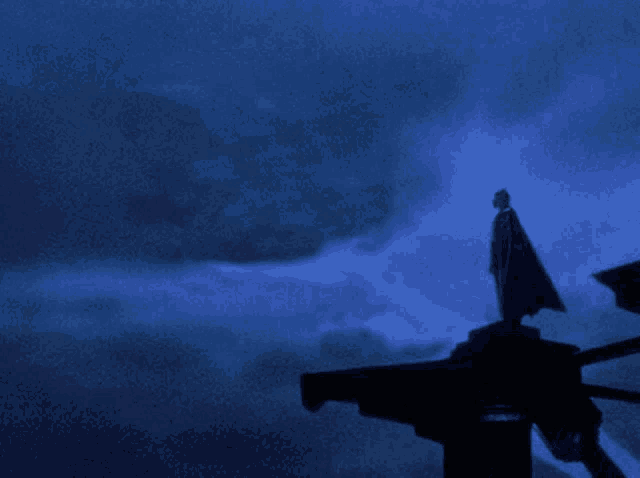 a man in a cape stands on top of a building with a silhouette of a bat flying in the sky
