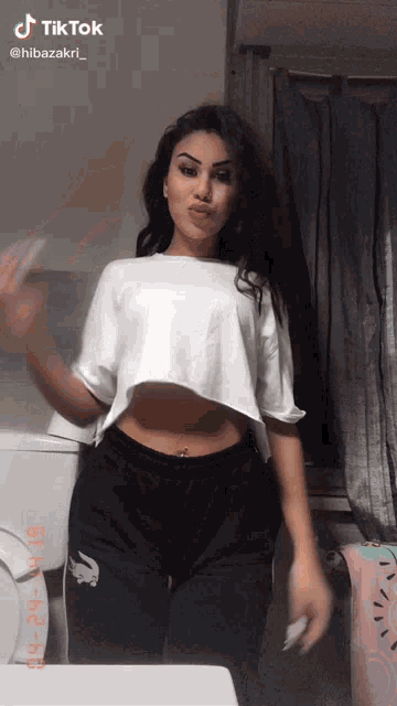 a woman in a white crop top and black sweatpants is standing in front of a toilet .