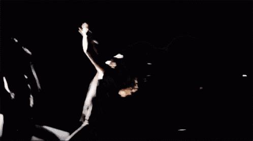 a woman is standing in a dark room with a lot of dust coming out of her hair .