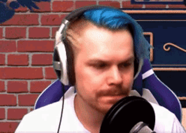a man with blue hair is wearing headphones in front of a brick wall