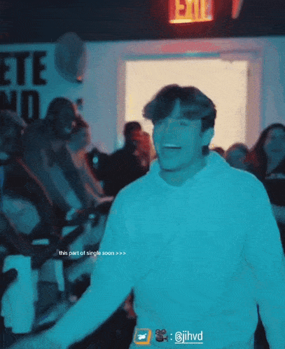 a man in a white hoodie is smiling in front of a red exit sign