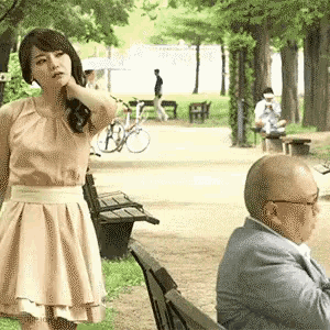 a woman in a pink dress is standing next to a man in a suit on a park bench .