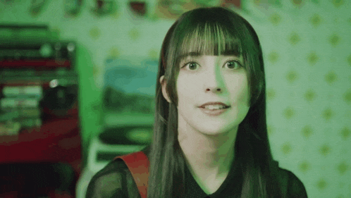 a young woman with long hair and bangs is standing in front of a green light .