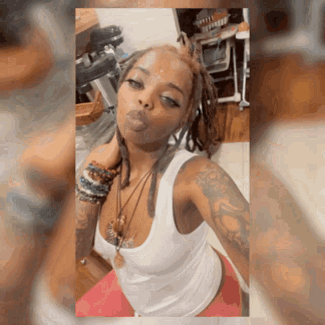 a woman with dreadlocks and a white tank top is taking a selfie