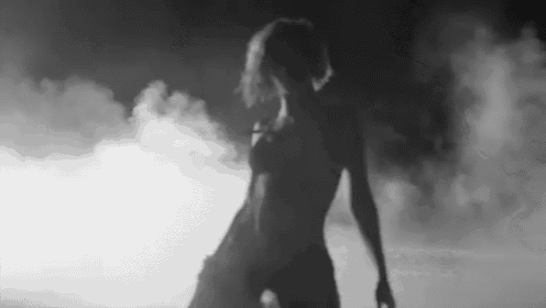 a black and white photo of a naked woman dancing in a dark room .