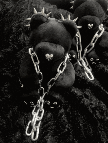a black teddy bear with spikes on its head is chained to a chain