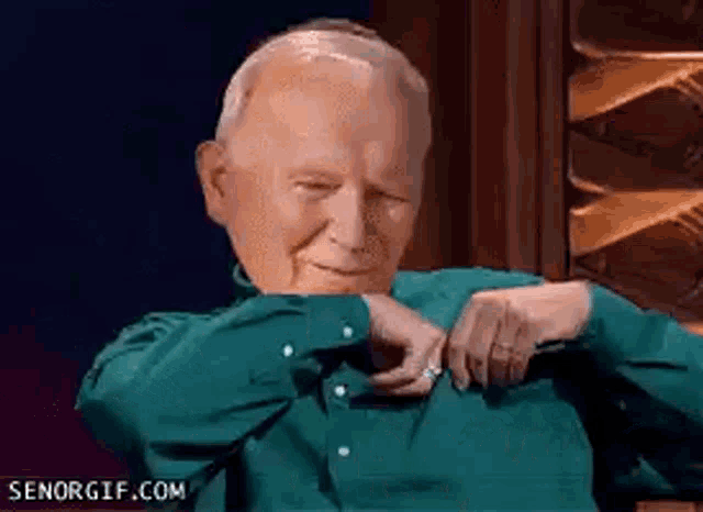 an older man in a green shirt is sitting in a chair with his eyes closed
