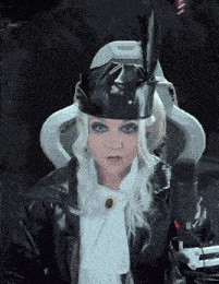 a woman sitting in front of a microphone wearing a black hat and a white scarf