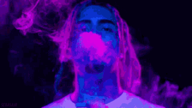 a man is smoking a cigarette in a dark room surrounded by purple and blue smoke .