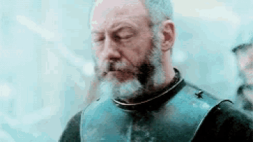 a man with a beard is wearing a blue armor and looking down .