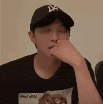 a man wearing a baseball cap and a t-shirt is covering his nose with his hand .
