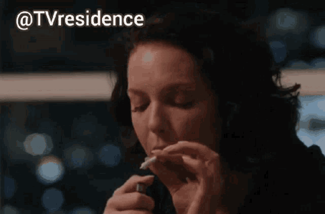 a woman is lighting a cigarette with a lighter in front of a window with the words @tvresidence above her