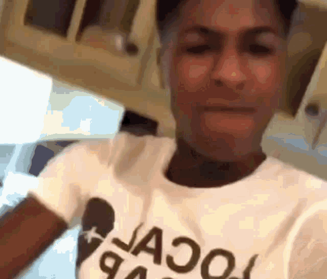 a man in a white t-shirt is making a funny face while sitting in a kitchen .