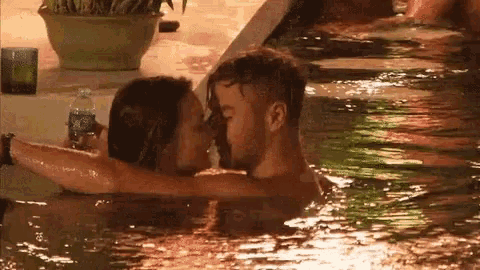a man and a woman kissing in a pool with a bottle of aquafina water in the background