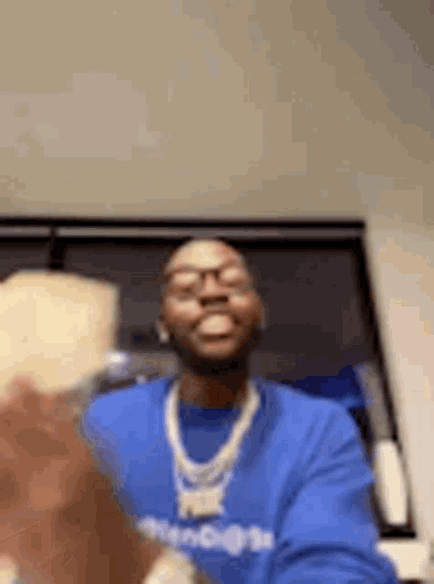 a man wearing a blue sweatshirt and a gold chain is holding a piece of cheese .