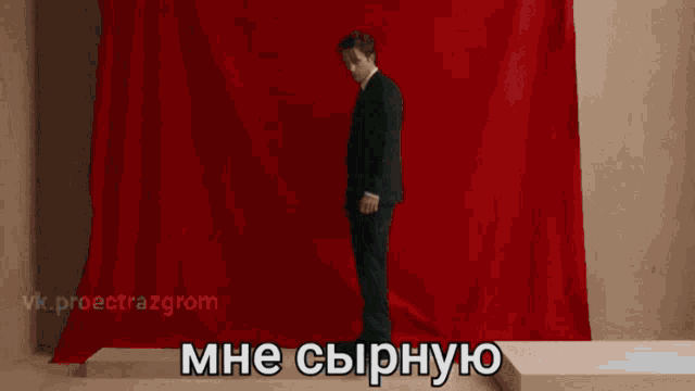 a man in a suit with his hands folded in front of a red background that says mne sypnyo