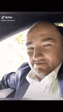 a man in a suit and white shirt is sitting in a car with tiktok written on the bottom right