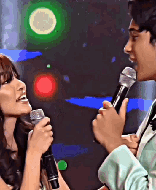 a man and a woman singing into microphones with a green light behind them