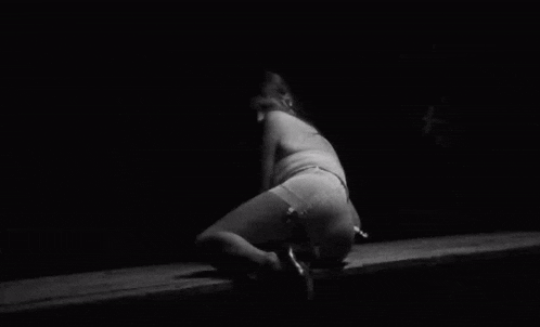 a black and white photo of a woman laying on the floor in a dark room .