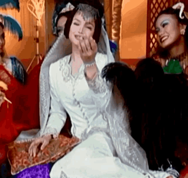 a woman in a white dress is sitting on a couch with other people