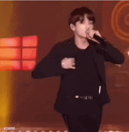 a young man is standing on a stage holding a microphone and singing into it .