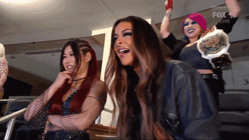 a group of women are sitting in a stadium watching a wrestling match and one of them is wearing a championship belt .
