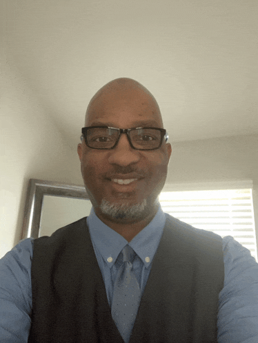 a man wearing glasses and a blue shirt smiles for the camera