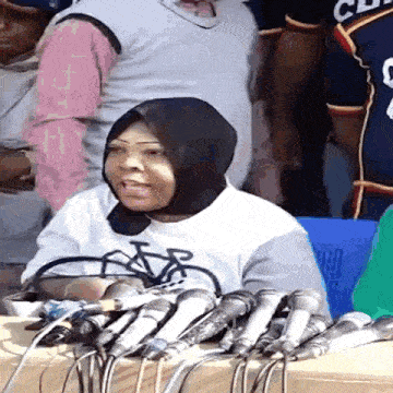 a woman wearing a bicycle shirt is sitting at a table with microphones