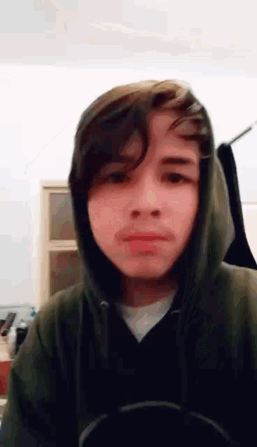 a young boy wearing a green hoodie is making a funny face .