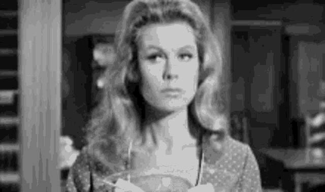 a black and white photo of a woman standing in a room holding a bowl .