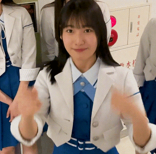 a girl wearing a white jacket and blue dress is giving a thumbs up sign