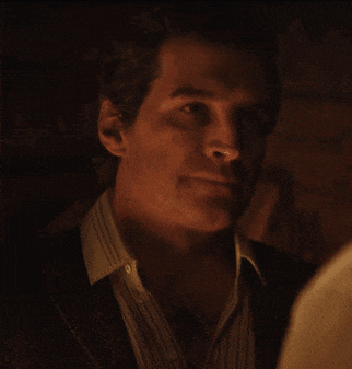 a man in a suit and striped shirt looks at the camera in a dark room