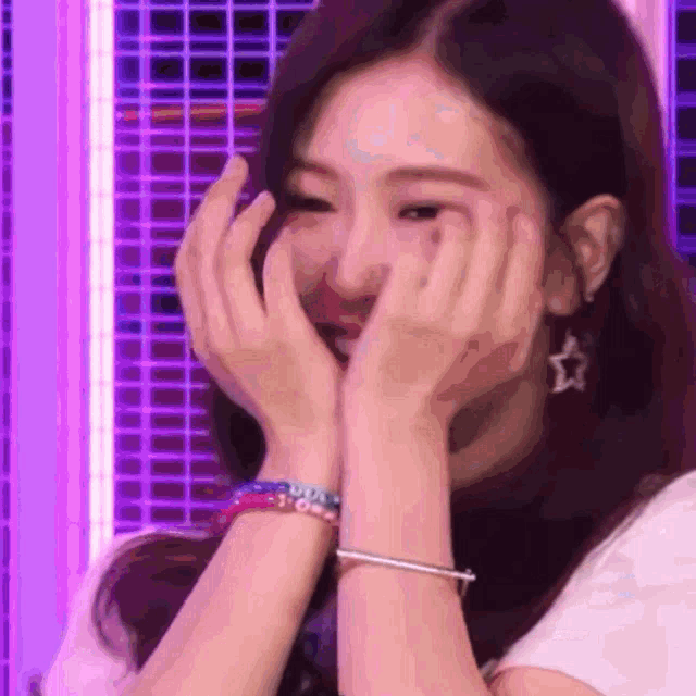 a woman covering her face with her hands while wearing a bracelet and earrings .