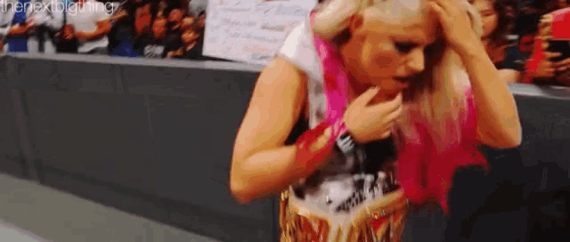 a woman with pink hair is standing in front of a crowd and holding her hair .