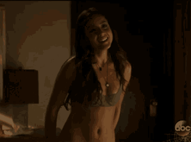 a woman in a bra is standing in a dark room with abc written on the bottom right