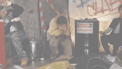 a man sits in front of a barrel that says danger explosifs
