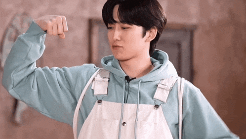 a young man in overalls is flexing his arm