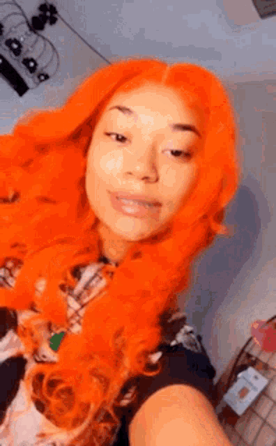 a woman with bright orange hair is taking a selfie with her phone .