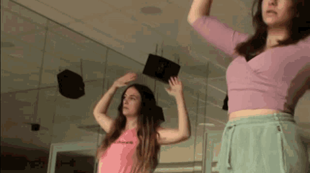 two women are dancing in front of a mirror and one of them is wearing a pink shirt that says ' shawn ' on it
