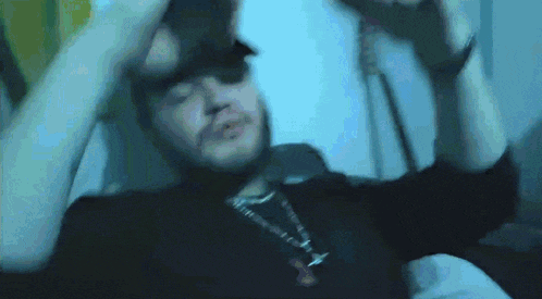 a man with a beard and a necklace is laying in bed with his hands on his head