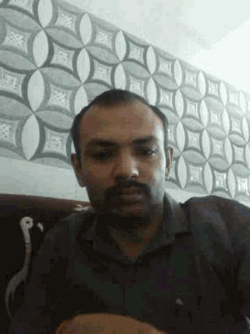 a man with a beard is sitting in front of a wall with a pattern on it