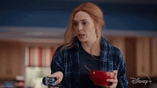 a woman in a plaid shirt is holding a bowl of cereal and a remote control with the disney logo in the background