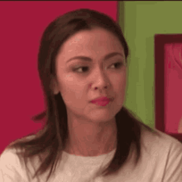 a woman is making a funny face while sitting in front of a pink wall .