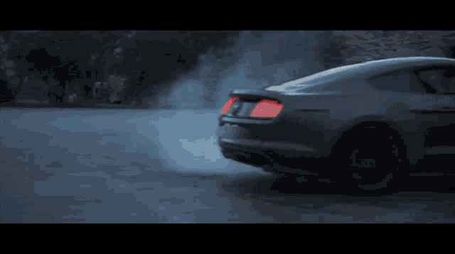 a ford mustang driving down a road with smoke coming out of the back