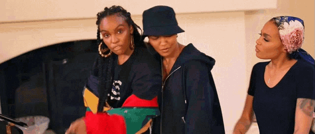 three women standing next to each other with one wearing a black bucket hat and a sweatshirt that says los angeles