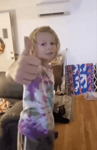 a young girl is giving a thumbs up in a living room .