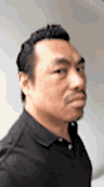 a man with a mustache and a black shirt is looking at the camera .