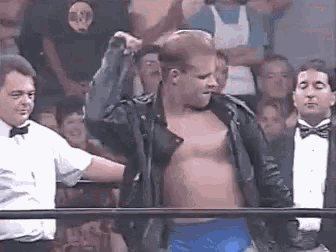 a man without a shirt is standing in a wrestling ring with his hands in the air .
