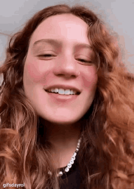 a woman with long red hair is smiling and wearing a pearl necklace